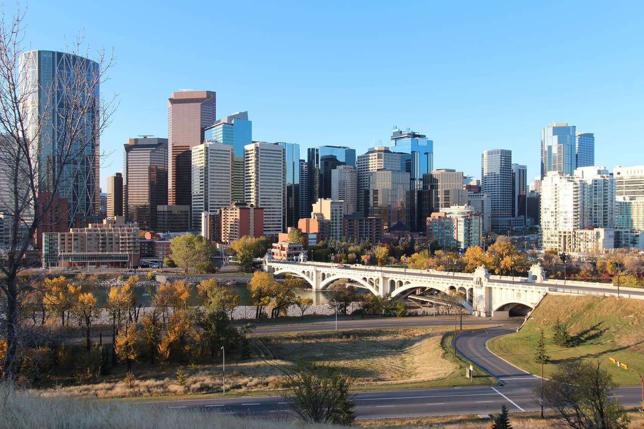 Downtown Calgary towers rising behind the Centre Street Bridge over the Bow River, with yellow autumn trees along Memorial Drive.