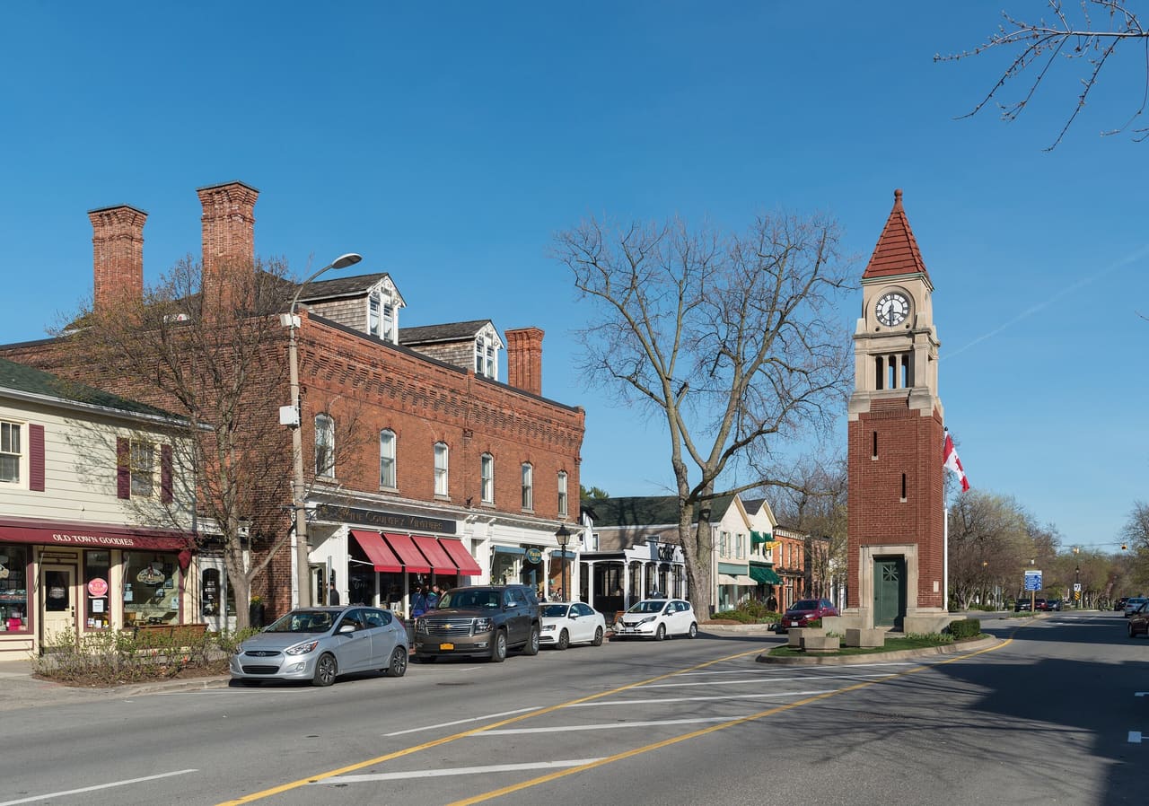 Queen Street in Niagara-on-the-Lake, with brick storefronts and the Clock Tower cenotaph under a clear spring sky.