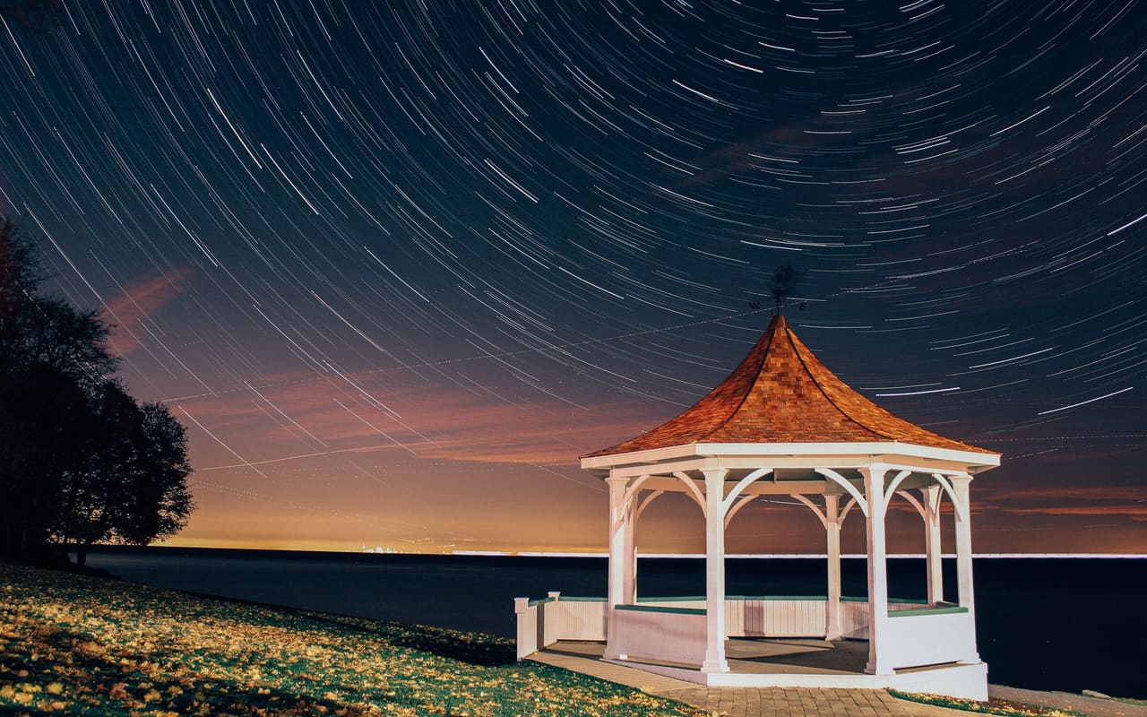 Star trails circling above a lit gazebo on the Lake Ontario shore at Niagara-on-the-Lake.