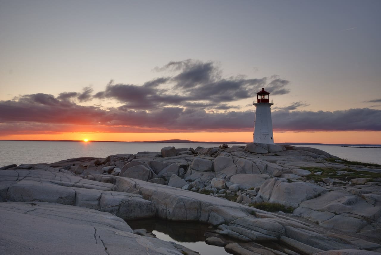 Peggy's Cove lighthouse on bare granite at sunset, with clouds over the Atlantic.