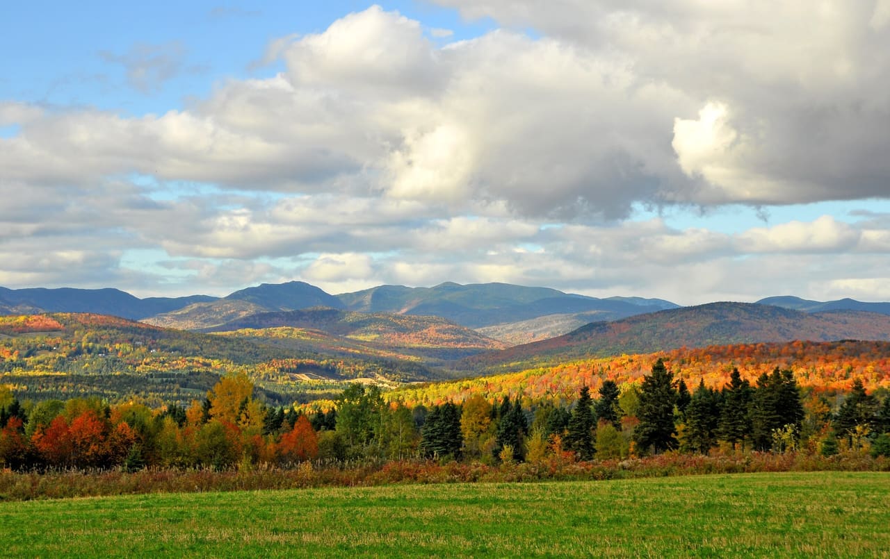 Rolling Charlevoix hills in autumn colour south of Baie-Saint-Paul, under large white clouds.