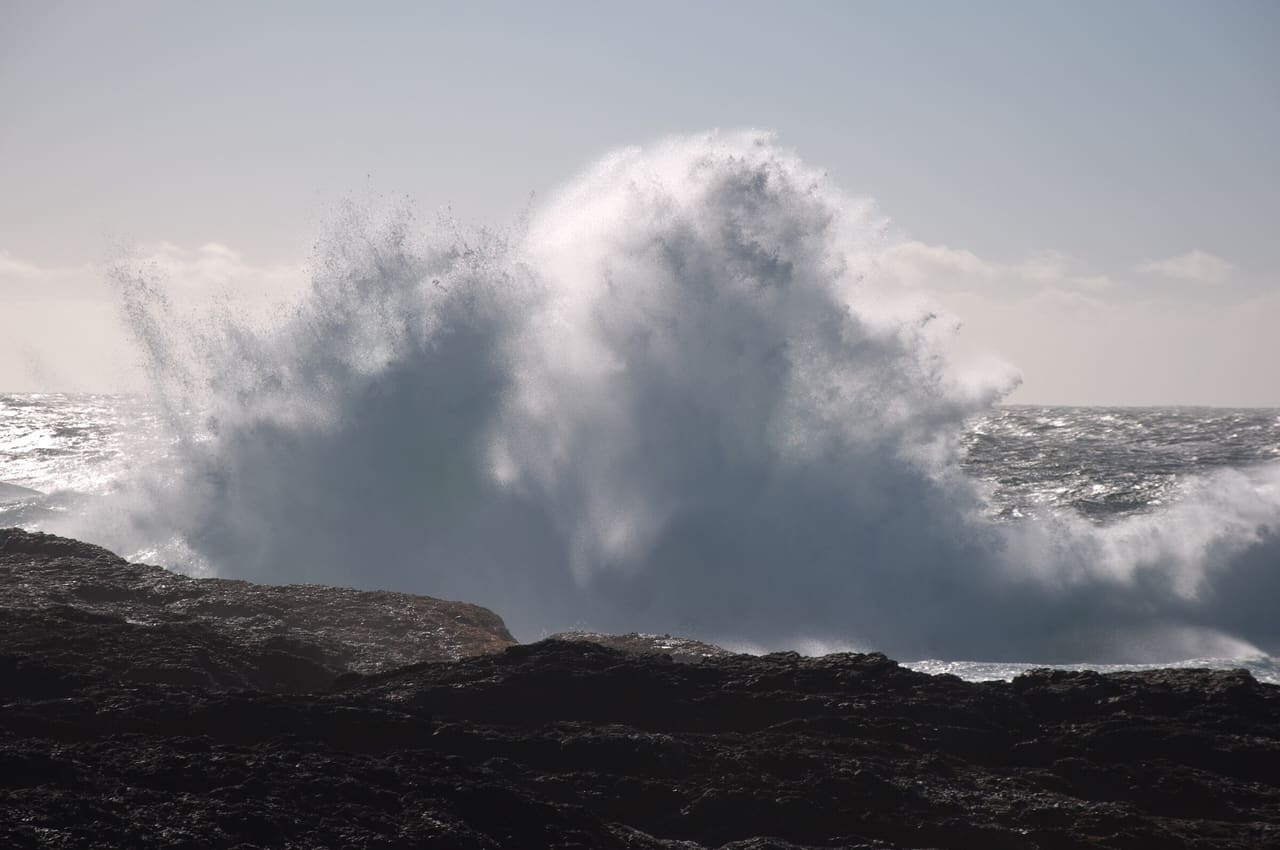 A storm wave bursting against dark rocks at Chesterman Beach near Tofino.