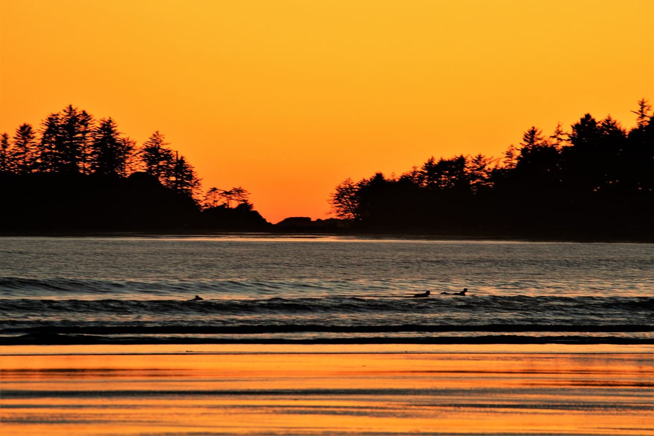 Sunset over a beach in Pacific Rim National Park Reserve near Tofino, with forested headlands in silhouette against an orange sky.