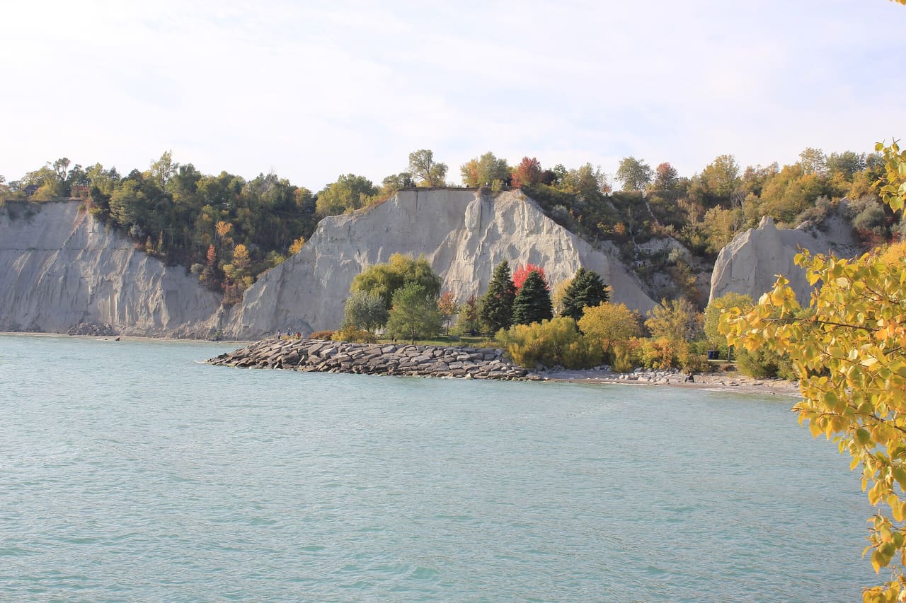 Pale cliffs of the Scarborough Bluffs above Lake Ontario, topped with trees turning autumn colours.