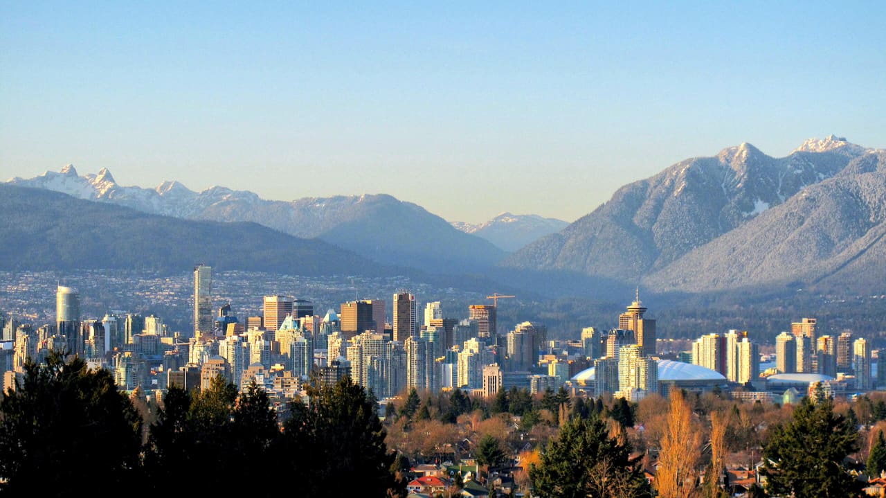 Downtown Vancouver towers seen from Queen Elizabeth Park, with the snow-dusted North Shore Mountains behind in late-afternoon light.