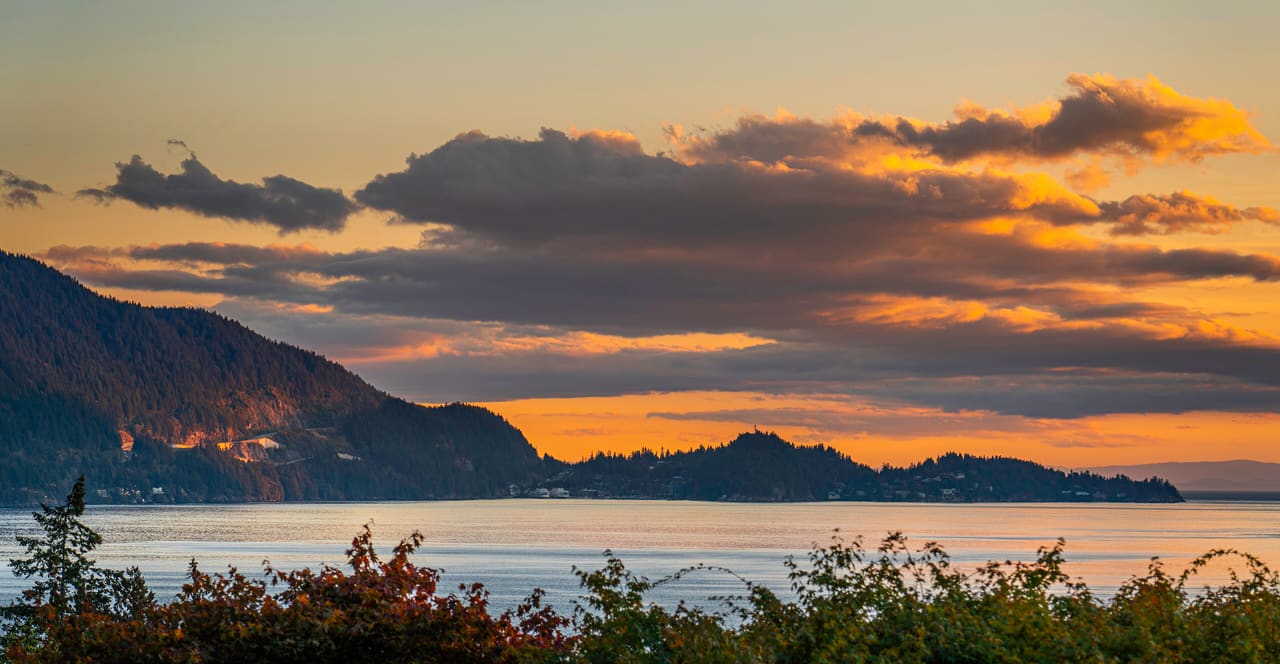 Sunset clouds over Howe Sound, with a dark forested headland on the left and low islands across calm water.